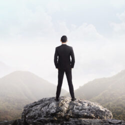 A business leader standing on a mountain peak, symbolising visionary leadership.