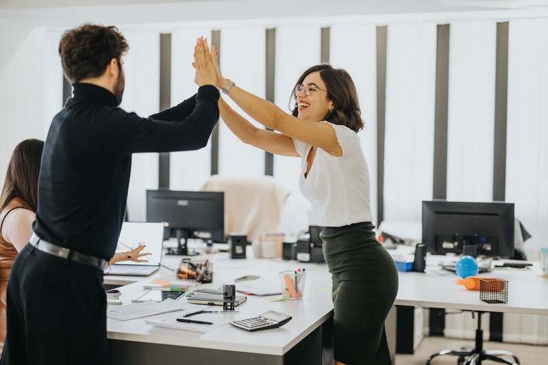  group of business professionals high-fiving in an office, celebrating teamwork and successful adaptation to change.