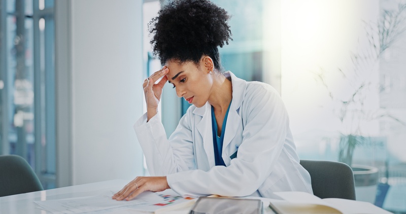 A stressed health business owner sitting at a desk, overwhelmed with paperwork and scheduling.